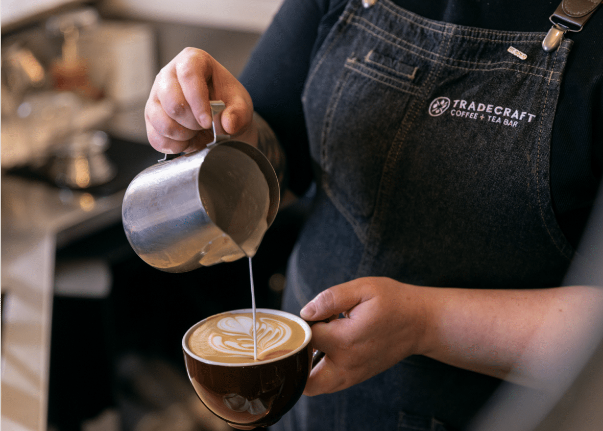 Barista pouring latte art while wearing a Tradecraft apron