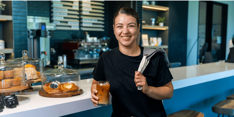 Barista smiling and holding coffee with an apron thrown over her shoulder