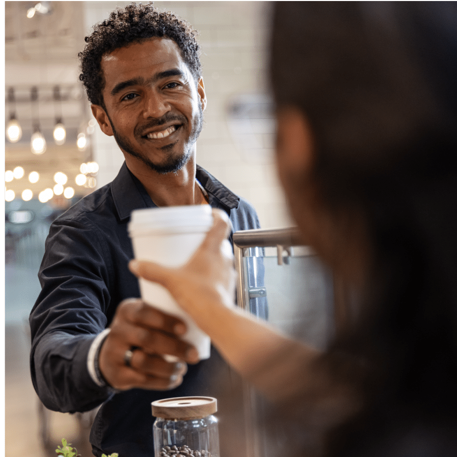 Male barista smiling and handing coffee to a customer