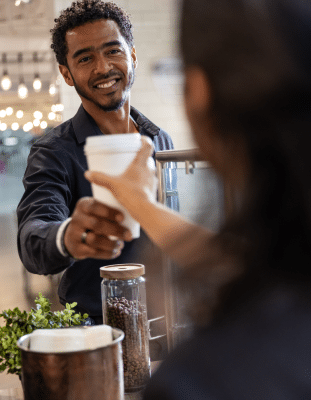 Male barista smiling and handing a customer a cup of coffee