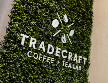 Tradecraft Coffee & Tea Lab Logo on a green plant wall