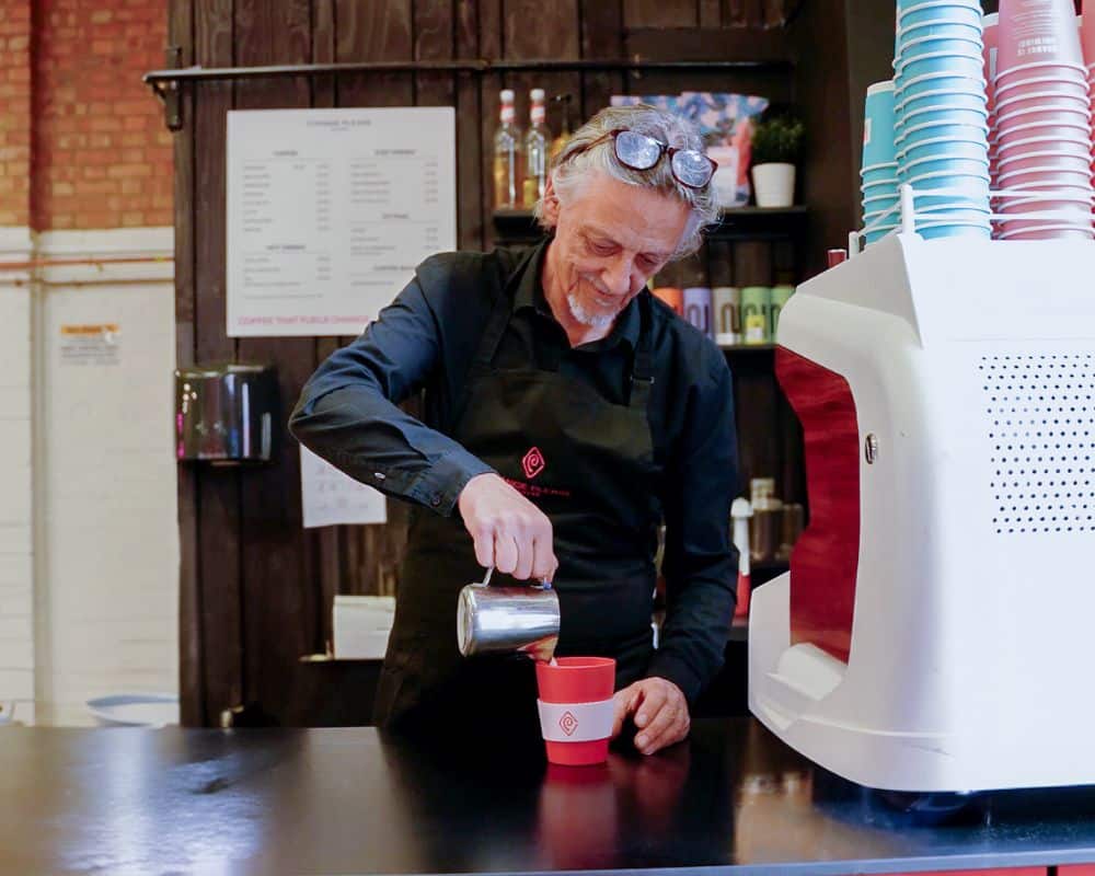 Male Change Please barista pouring coffee into a cup behind the counter