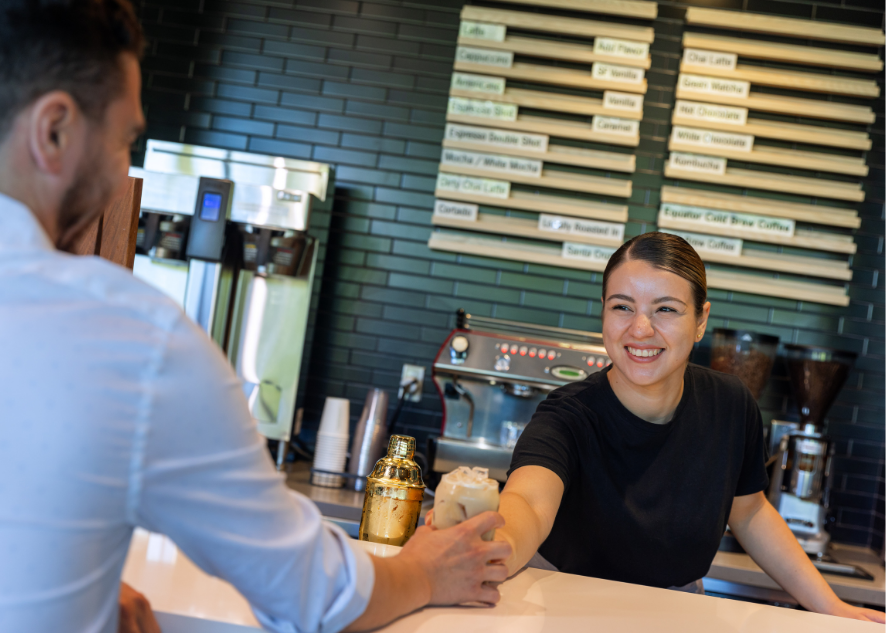 Female barista smiling and sliding iced coffee across the counter to a customer