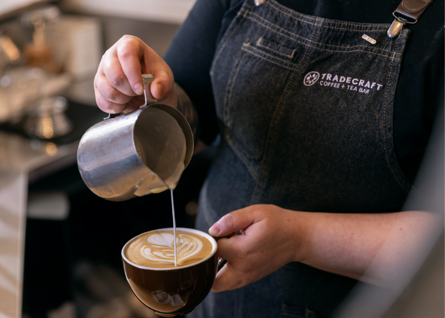 Barista pouring latte art while wearing a Tradecraft apron
